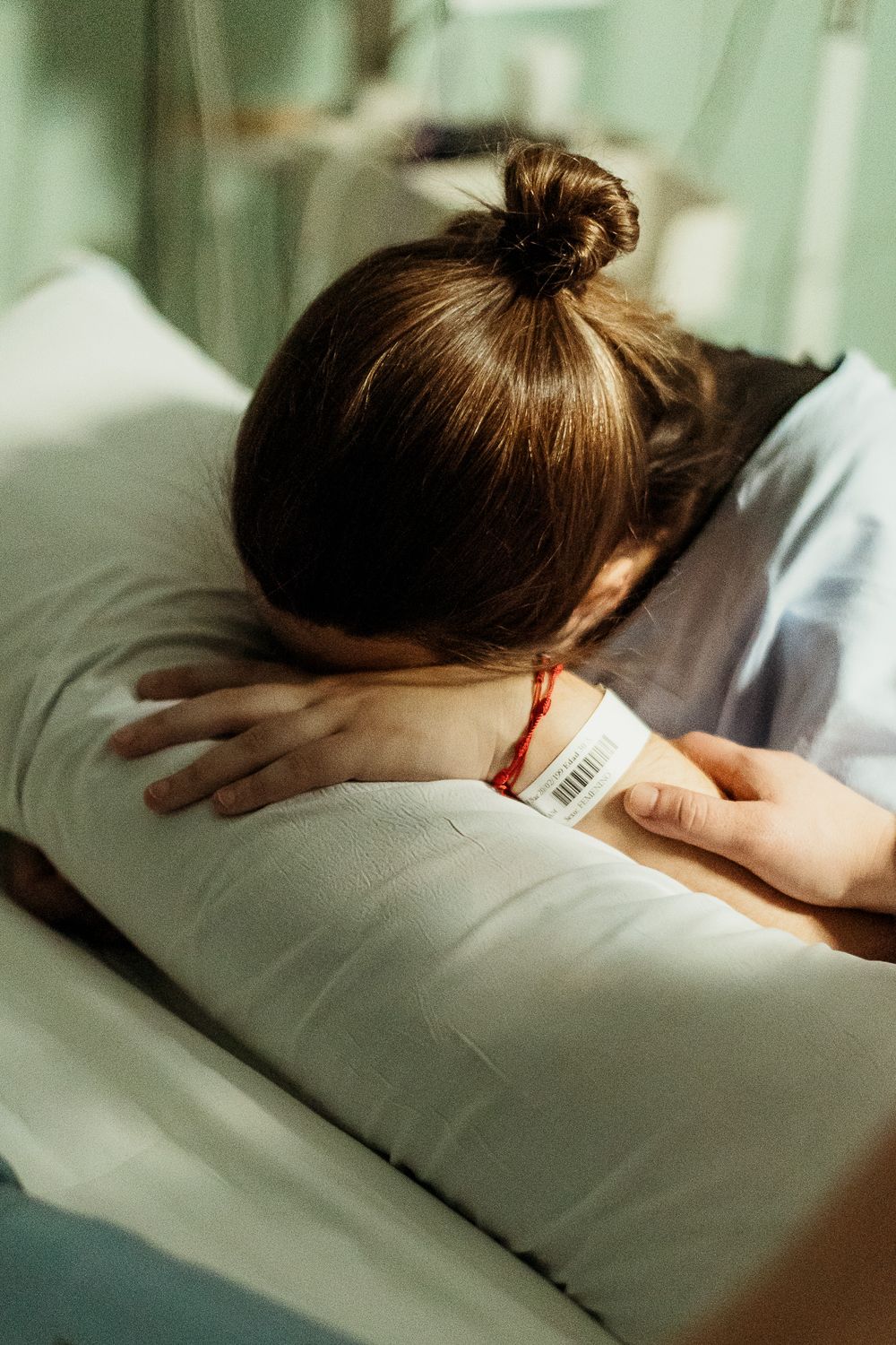 Patient with brown hair in a bun resting on a hospital pillow, wearing a medical ID wristband.