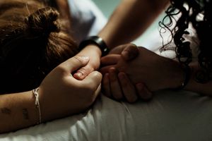 Two people holding hands tenderly on a white surface, showing comfort and emotional support.