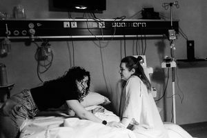 Black and white photo of a patient in a hospital bed being comforted by a caring visitor or nurse.