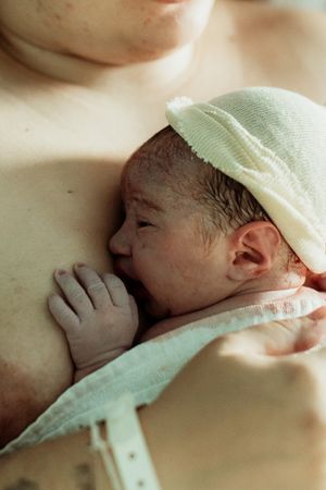 Newborn baby in green hat resting on mother's chest during skin-to-skin contact after birth.