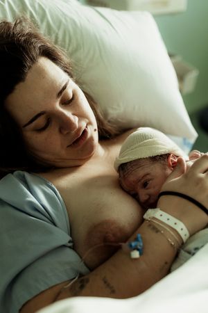 A new mother holds her newborn baby skin-to-skin in a hospital bed shortly after birth.