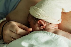 Newborn baby with white hat resting on mother's chest during skin-to-skin contact after birth.