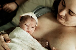 Newborn baby wrapped in white towel resting on mother's chest during skin-to-skin contact after birth.