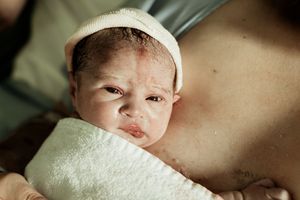 Newborn baby wrapped in white towel wearing knit hat, held against mother's chest after birth.
