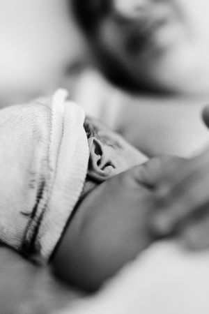 Black and white photo of a newborn baby wearing a hospital hat, cradled in a parent's arms.
