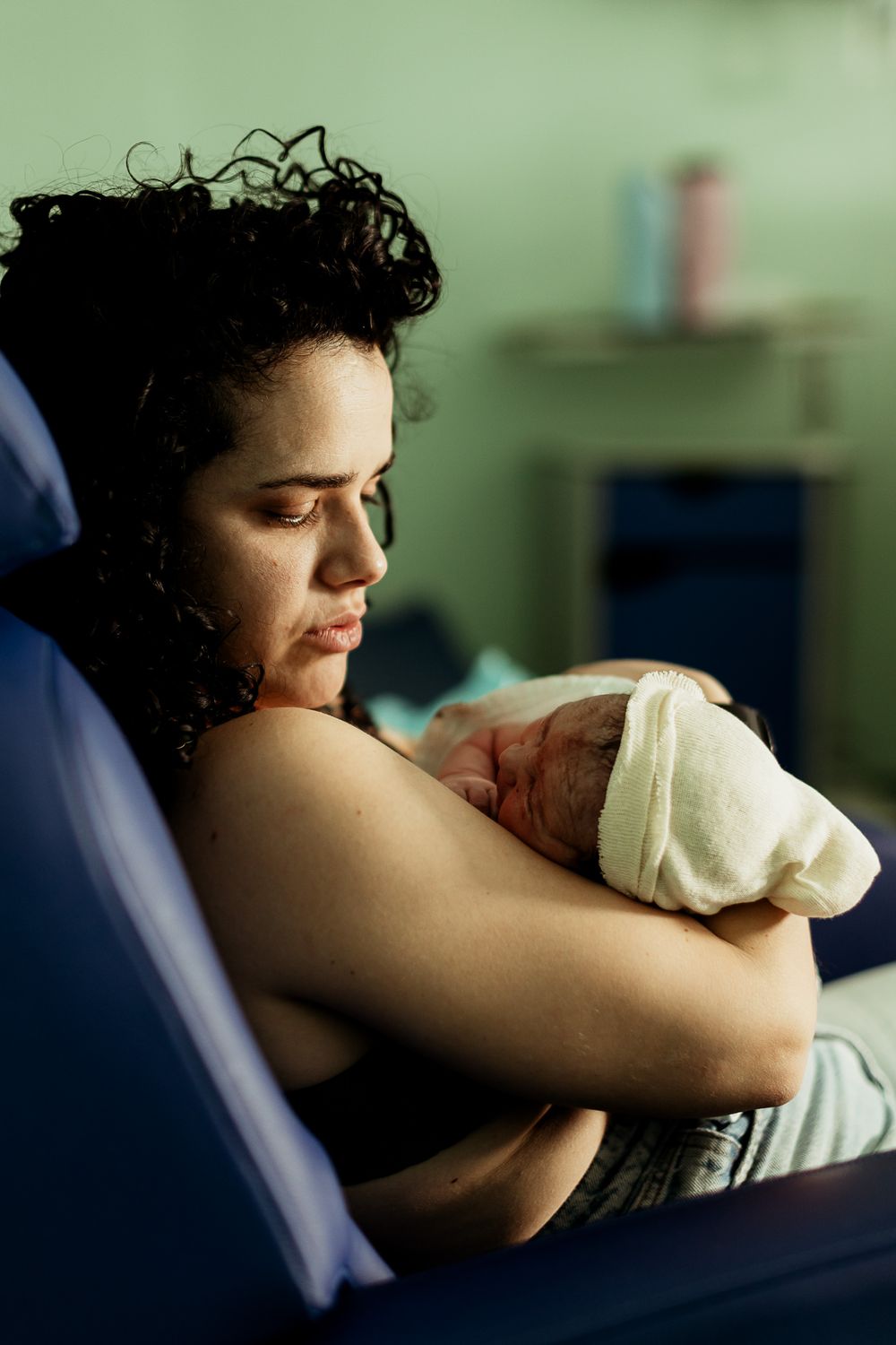 A new mother tenderly holds her newborn baby wrapped in a white towel in a hospital room.
