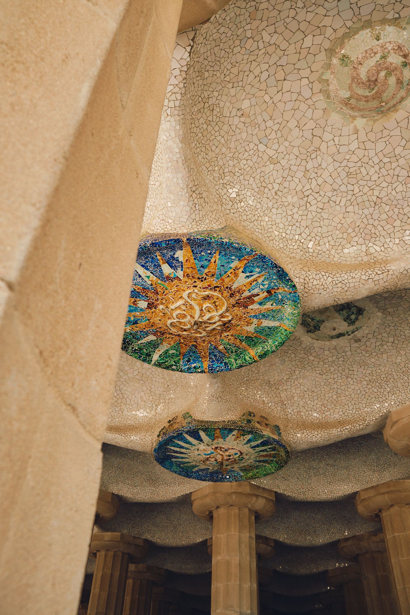 Colorful mosaic sun medallions decorating the ceiling of Park Guell, Barcelona, Gaudi architecture detail.