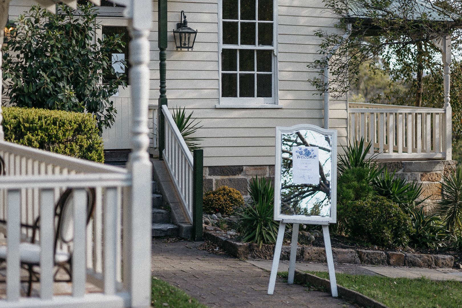 White easel with signage displayed outside a charming white heritage home with manicured gardens.
