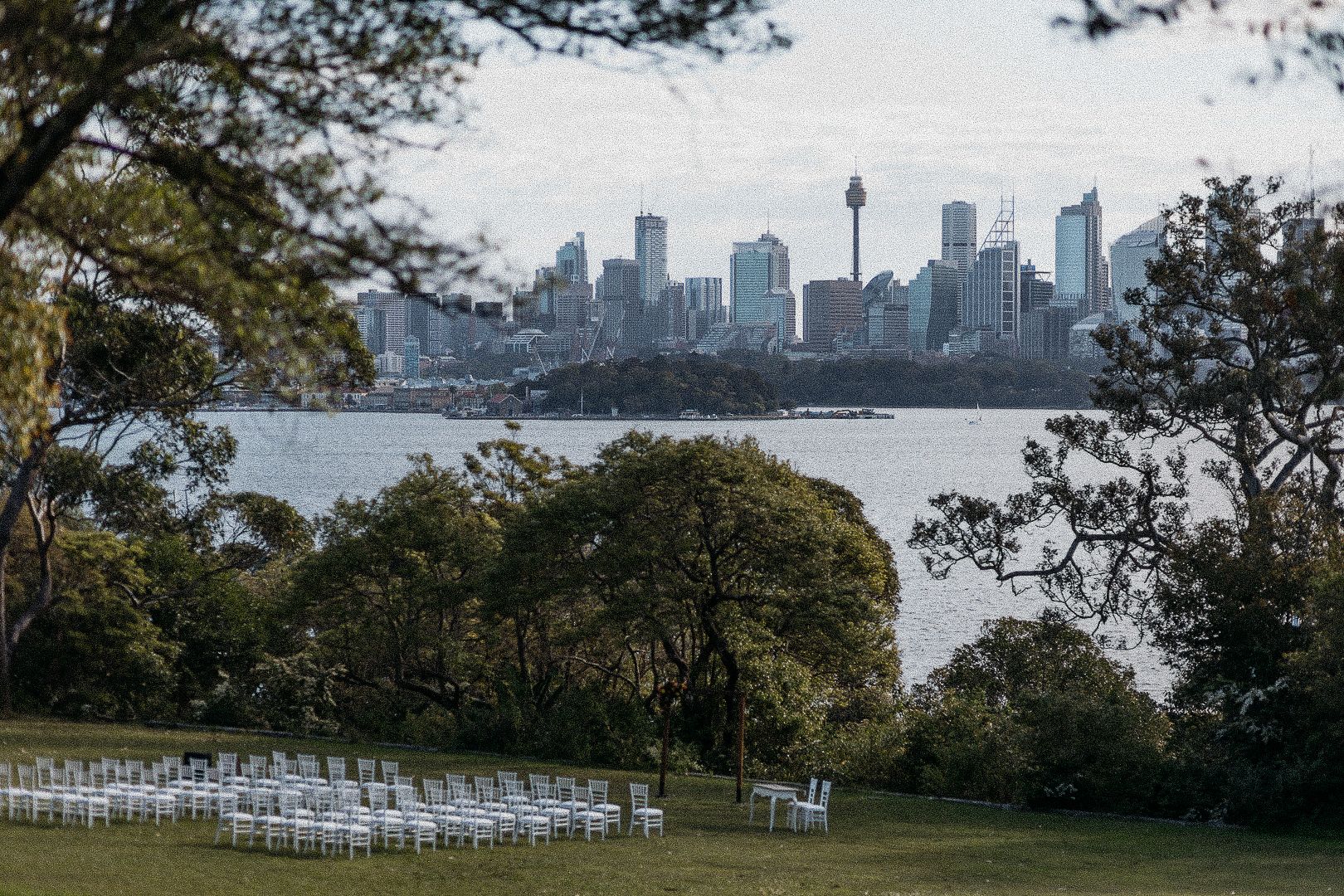 Outdoor wedding chairs set on green lawn with Sydney city skyline and harbor views in background.
