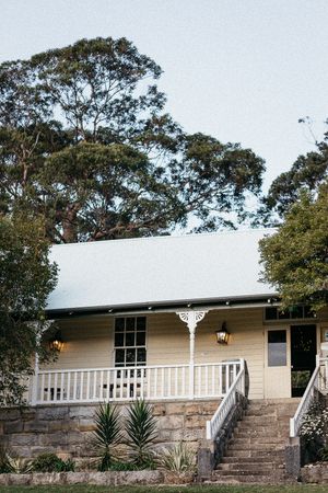 Charming yellow cottage with white porch railing, stone steps, and tall eucalyptus trees at dusk.