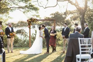 Outdoor wedding ceremony under wooden arch with floral decor, bride and groom exchanging vows at golden hour.