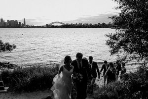 Black and white wedding photo of bride and groom walking along Sydney Harbour beach with iconic Harbour Bridge skyline backdrop.