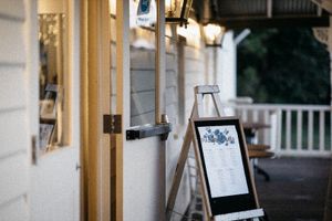 Outdoor restaurant entrance with a wooden menu board on an easel, warm string lights, and a white porch in the background.