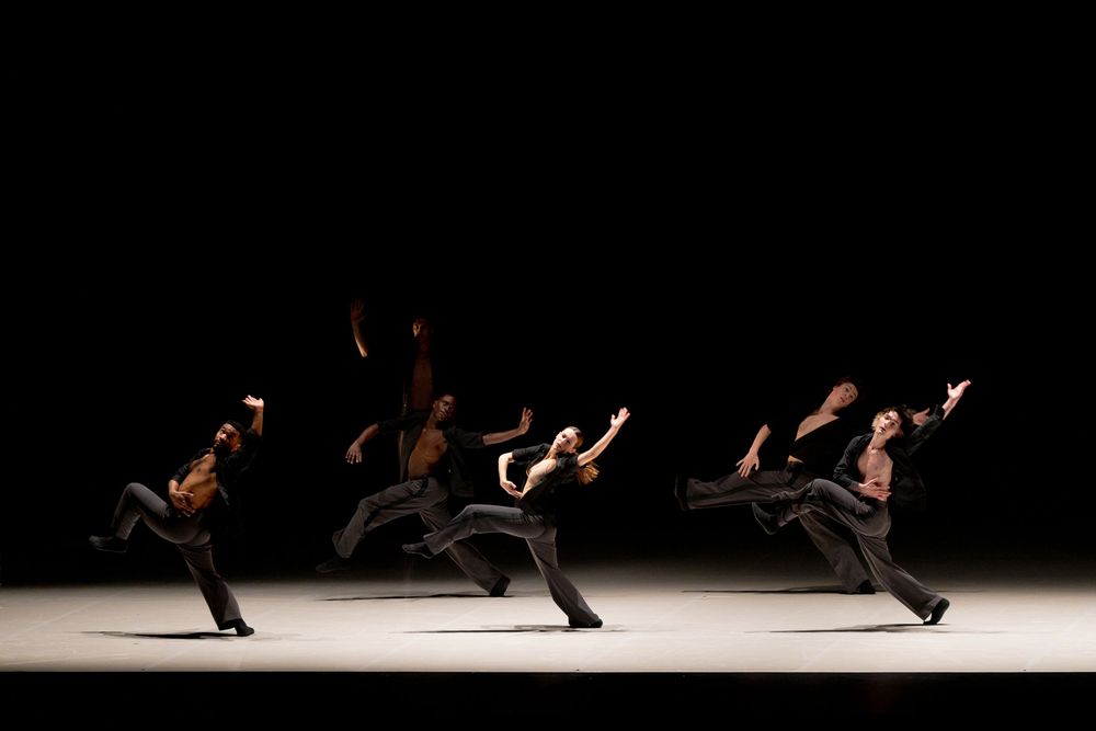 Dancers perform dynamic contemporary dance moves on a dimly lit stage with dramatic lighting.