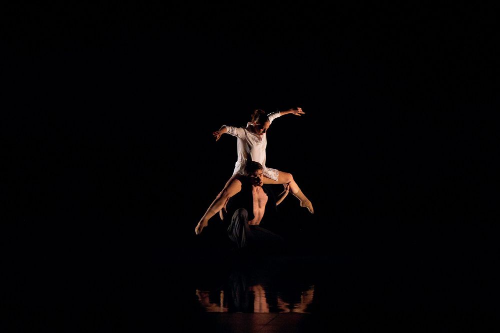 Two ballet dancers perform an elegant lift on a dark stage, showcasing graceful movement and artistic expression.