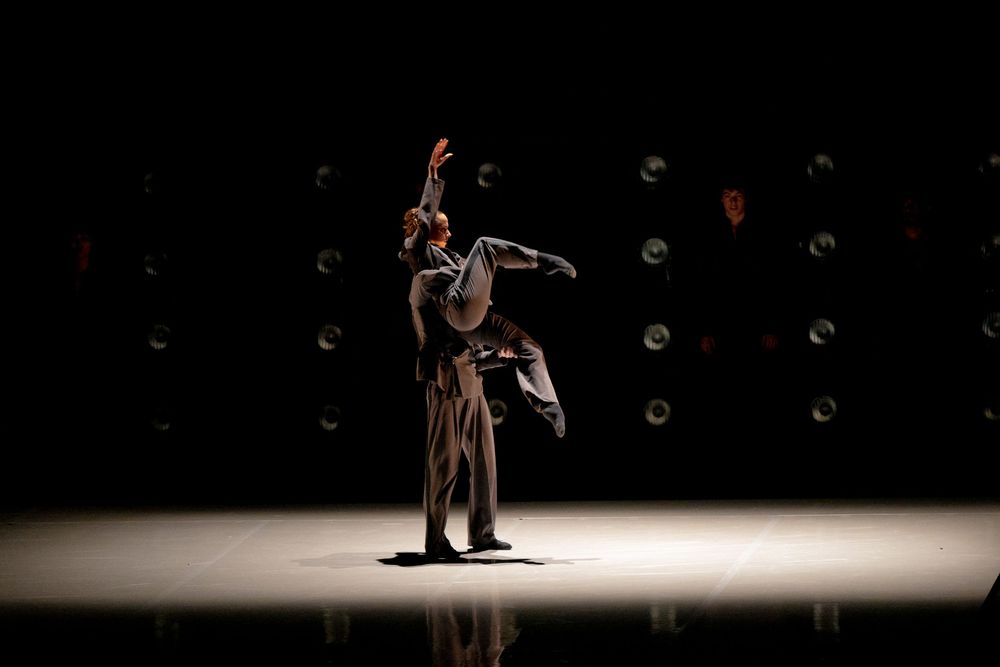 A solo dancer performs on a spotlight-lit stage with circular decorations in the dark background.