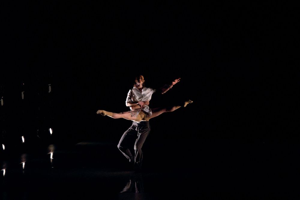 Two ballet dancers perform an elegant lift on a dark stage, showcasing graceful extensions and artistic choreography.