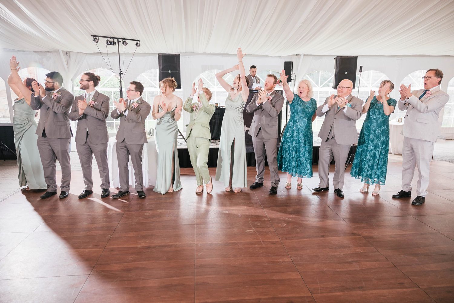 Full wedding party lined up on the dance floor, cheering and applauding as the newlyweds are announced.