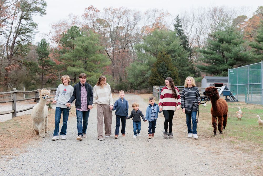 Family group walking with alpacas on a farm path surrounded by autumn trees.