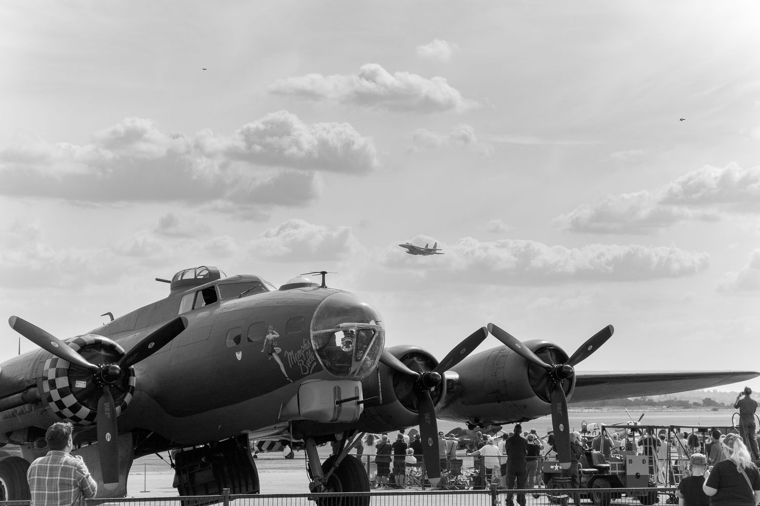Vintage WWII B-17 Flying Fortress bomber on display at an airshow with spectators and aircraft flying overhead.