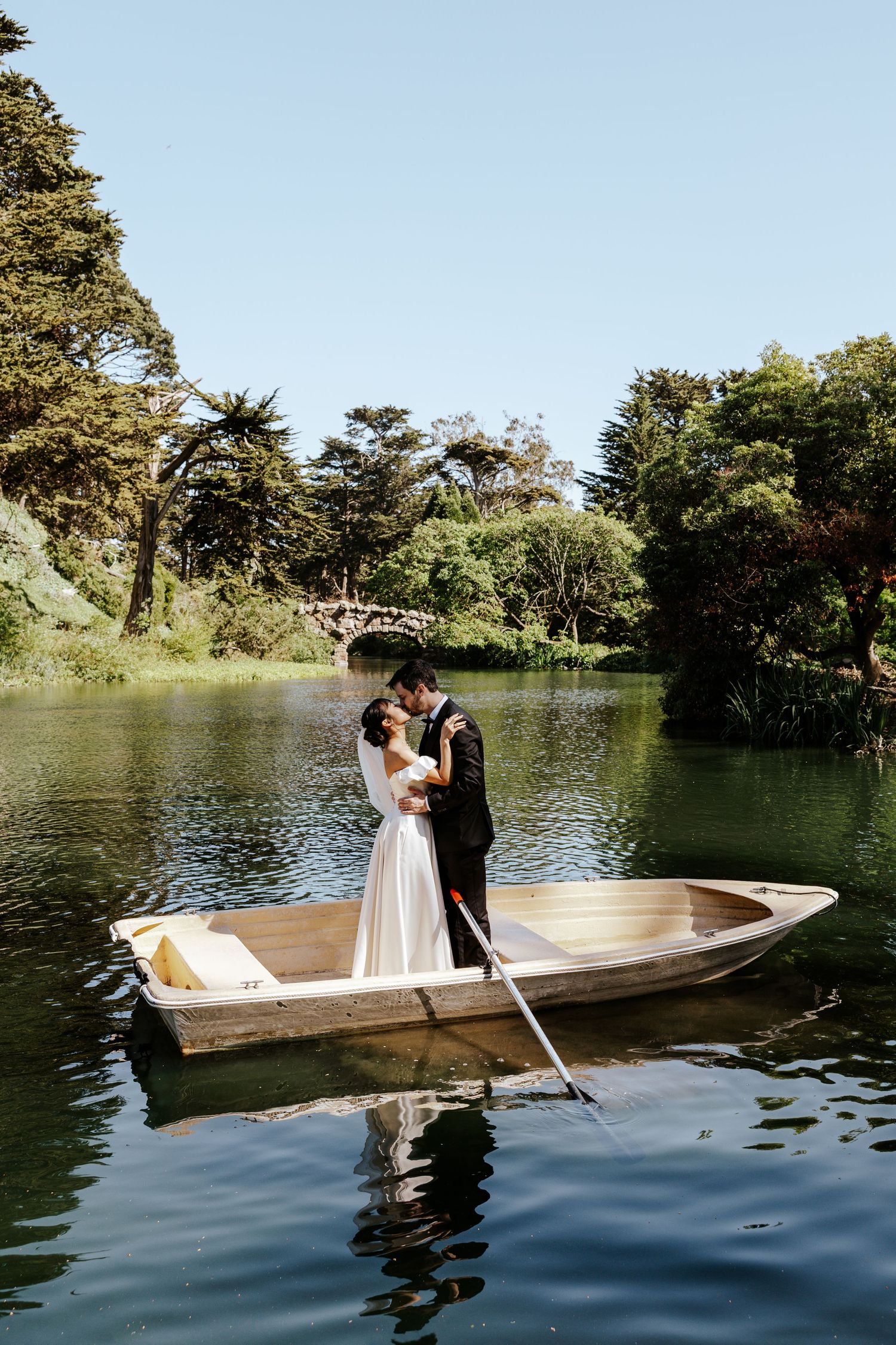 sf elopement couple kissing in row boat with stone bridge behind them on blue heron lake in golden gate park