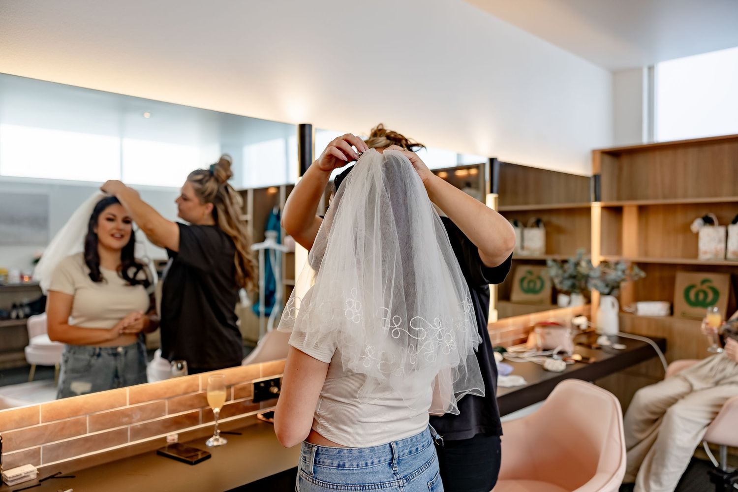 Bride having her wedding veil fitted in a modern bridal suite with mirror reflections.