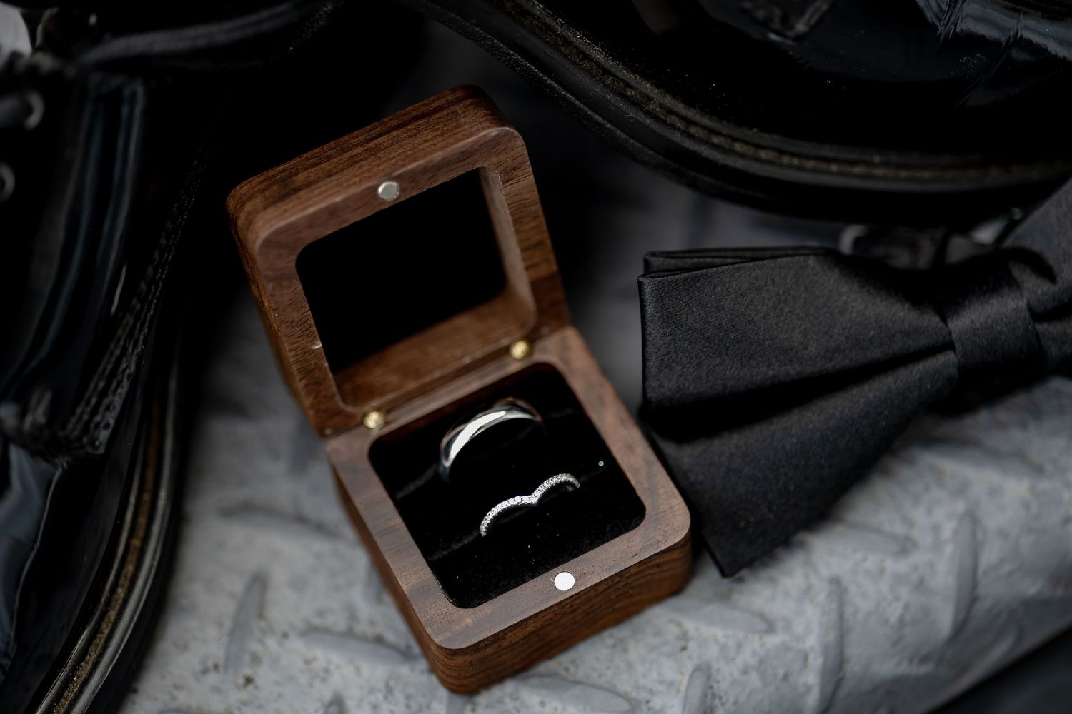 Two silver wedding bands displayed in an open wooden ring box on a dark fabric surface.