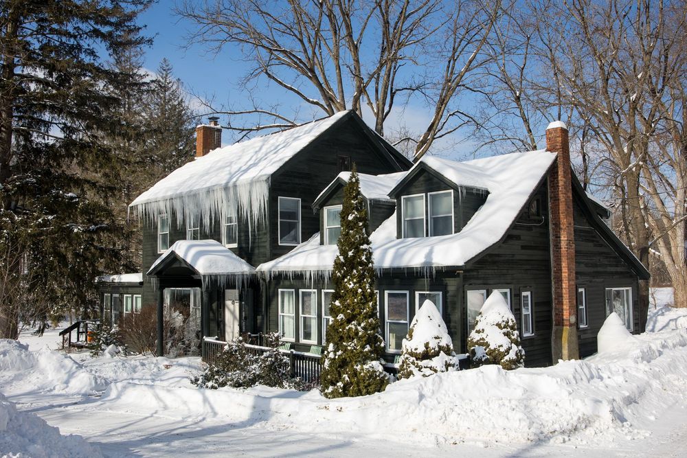 Dark green traditional home with dormers, brick chimneys, and Christmas tree surrounded by heavy snow.