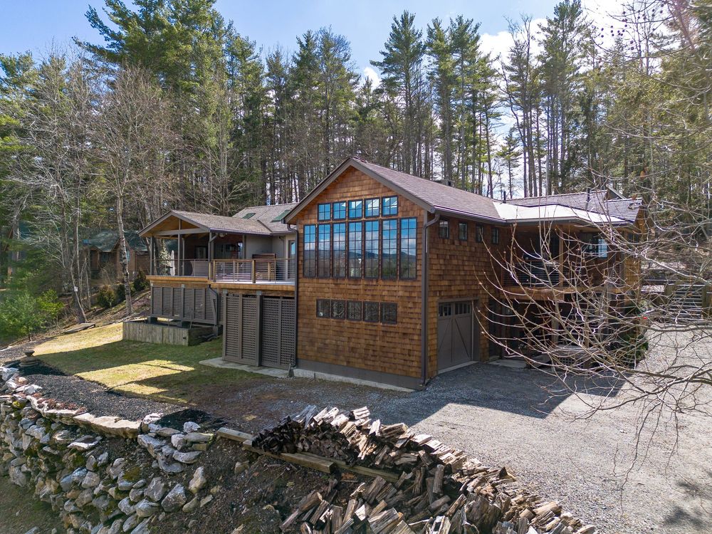 Cedar-sided chalet home with large windows and wraparound deck nestled among tall pine trees in spring.