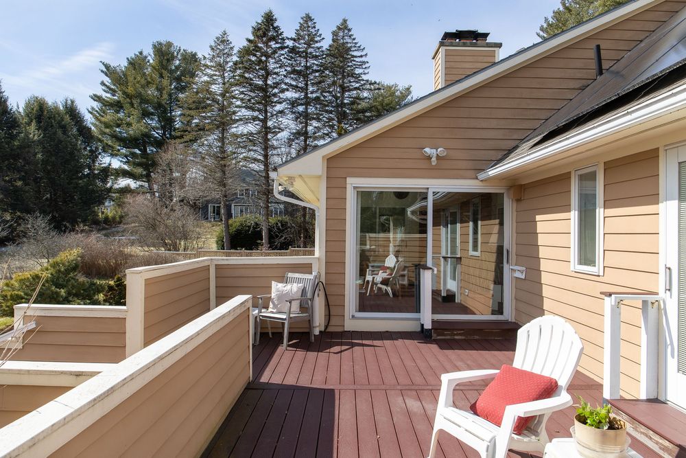 Beige home with composite deck featuring white Adirondack chairs and red accent pillow in early spring.