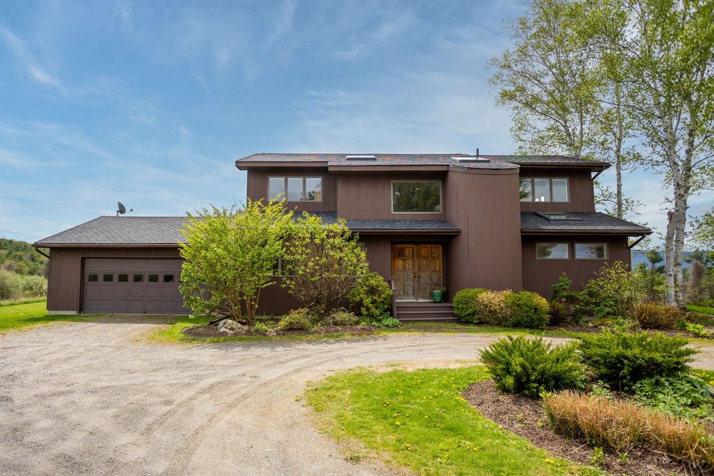 Modern brown two-story home with attached garage, solar panels, and landscaped driveway entrance.