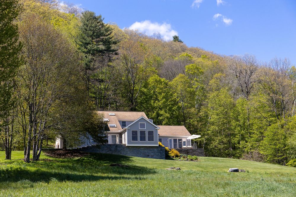 Charming cape-style home nestled on a green hillside surrounded by lush spring foliage.