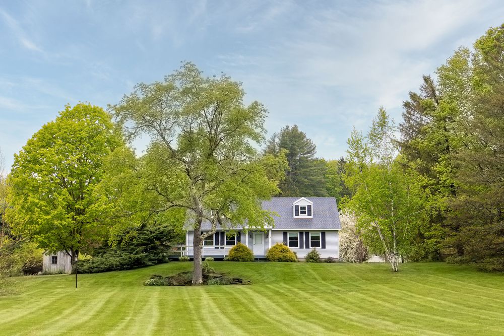 Classic cape cod home with manicured striped lawn and mature trees under a bright blue sky.
