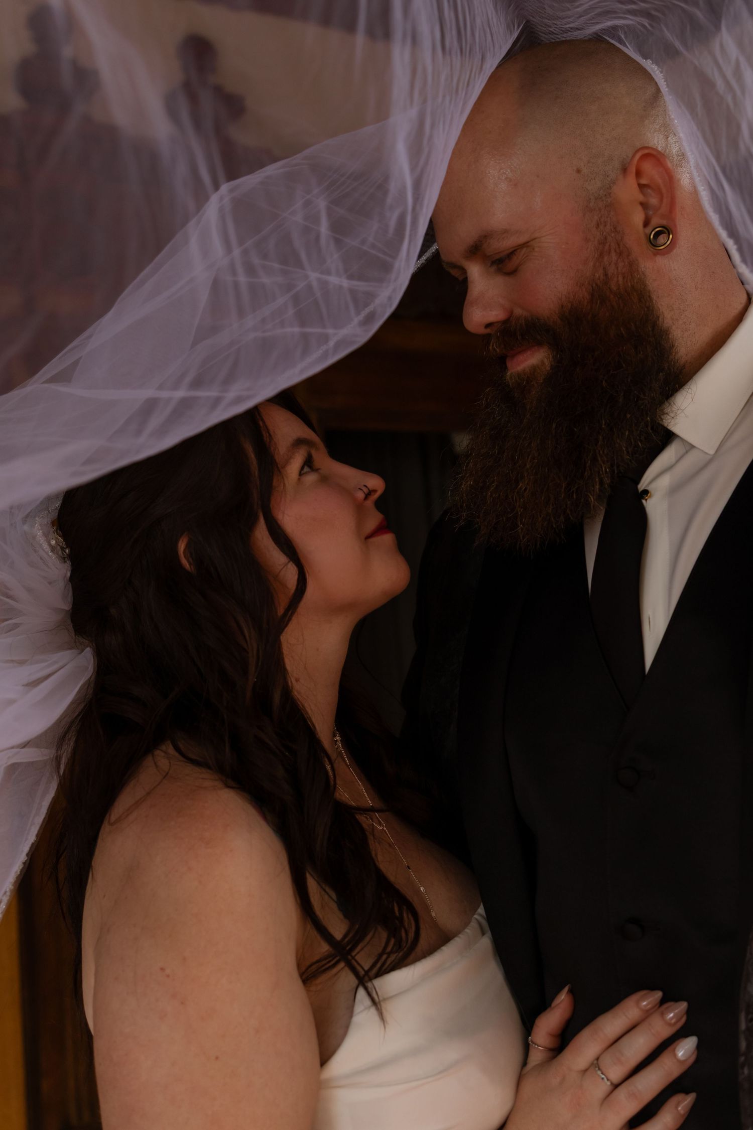 Bride and groom share an intimate moment under a flowing white veil, gazing lovingly at each other on their wedding day.