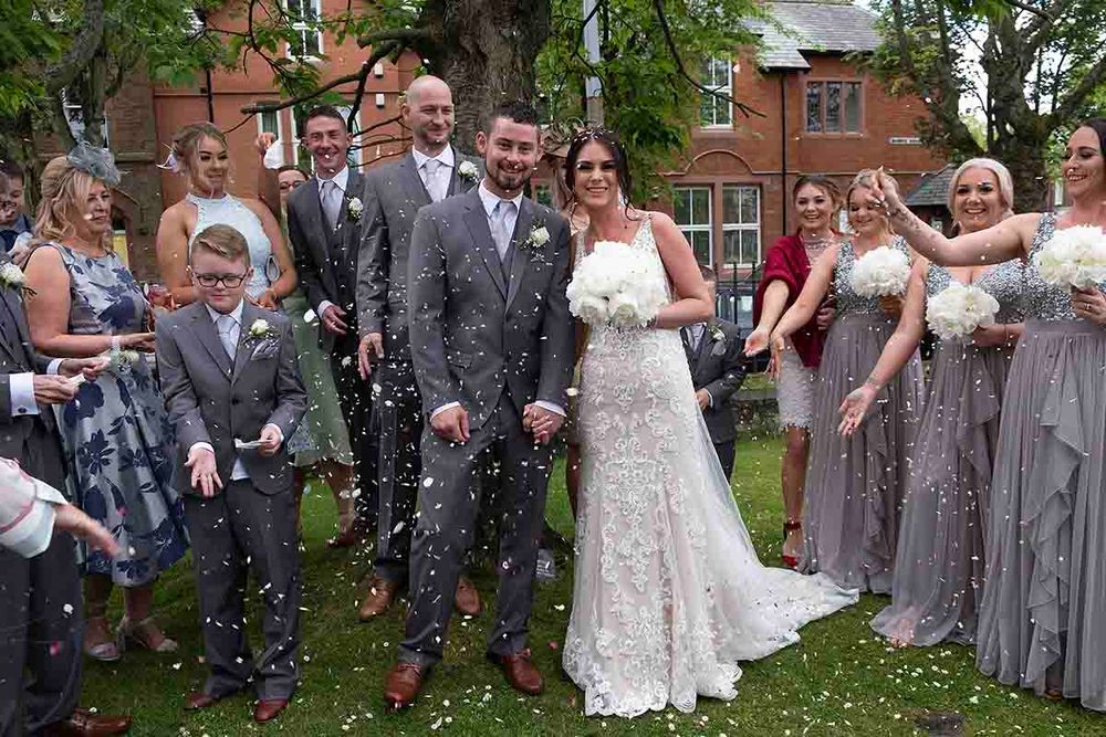 Bride and groom celebrate with wedding party as confetti falls outside the church prior to the wedding celebration at Greenhill Hotel