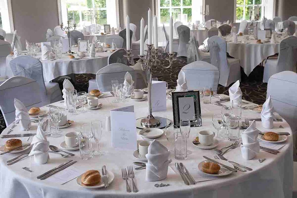 Elegantly set  tables with white linens, crystal glassware, and folded napkins in a bright wedding reception hall at Greenhill Hotel
