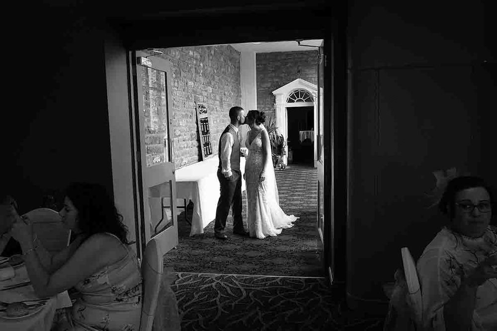 Black and white photo of a bride and groom sharing a kiss in a doorway at their wedding reception prior to the speeches at Greenhill