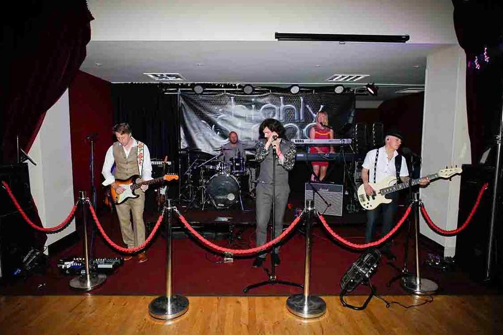 Live band performing on stage with red rope barriers, guitarist, vocalist, bassist, and drummer at Greenhill Hotel wedding venue.
