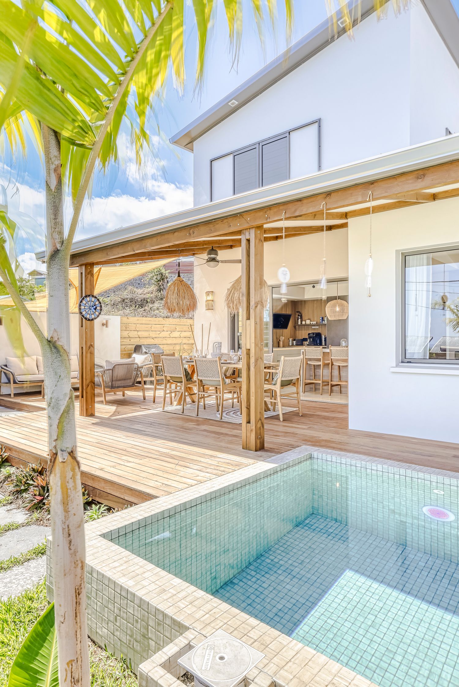 Luxurious outdoor patio with white built-in seating, fire pit, lush green lawn, and tropical palm trees in Miami.