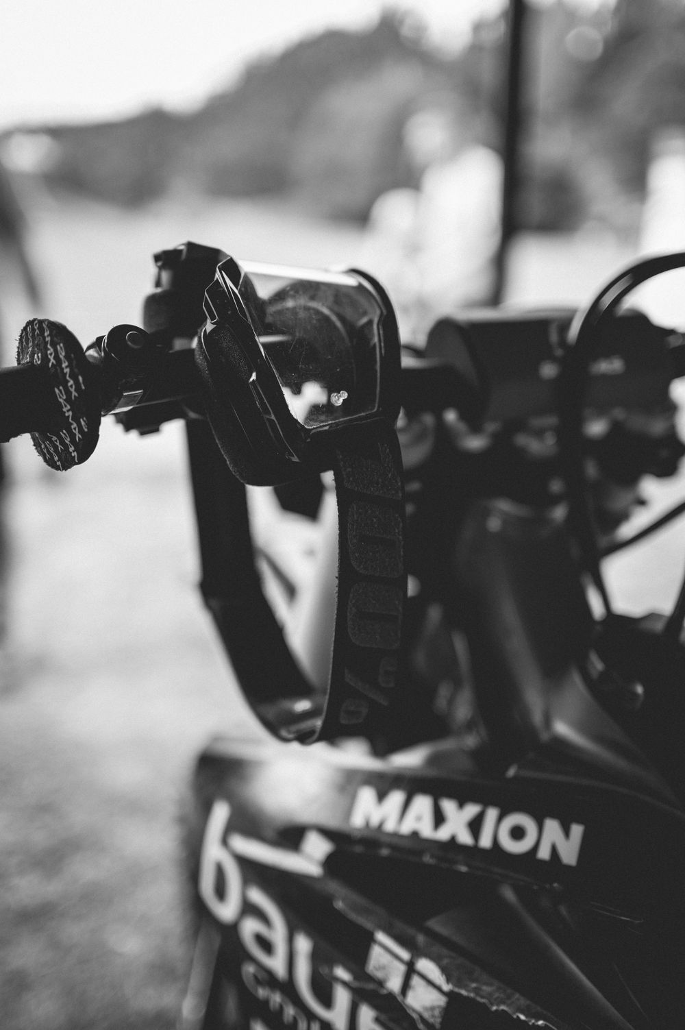 Black and white close-up of a Maxion bike rack with secured bicycle handlebar straps in an outdoor setting.