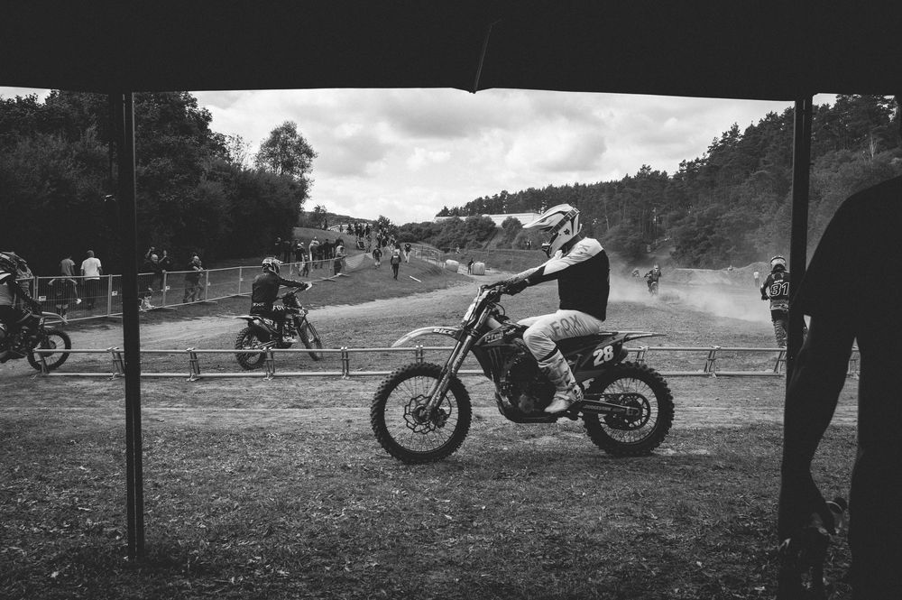 Black and white photo of a motocross rider on a dirt bike at an outdoor racing event with spectators.