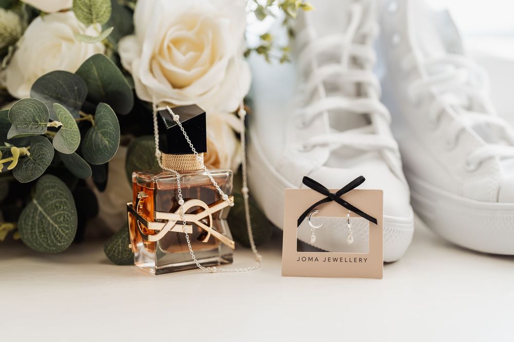 Bridal flat lay featuring YSL perfume, Joma Jewellery earrings, white Converse sneakers, and fresh white roses.