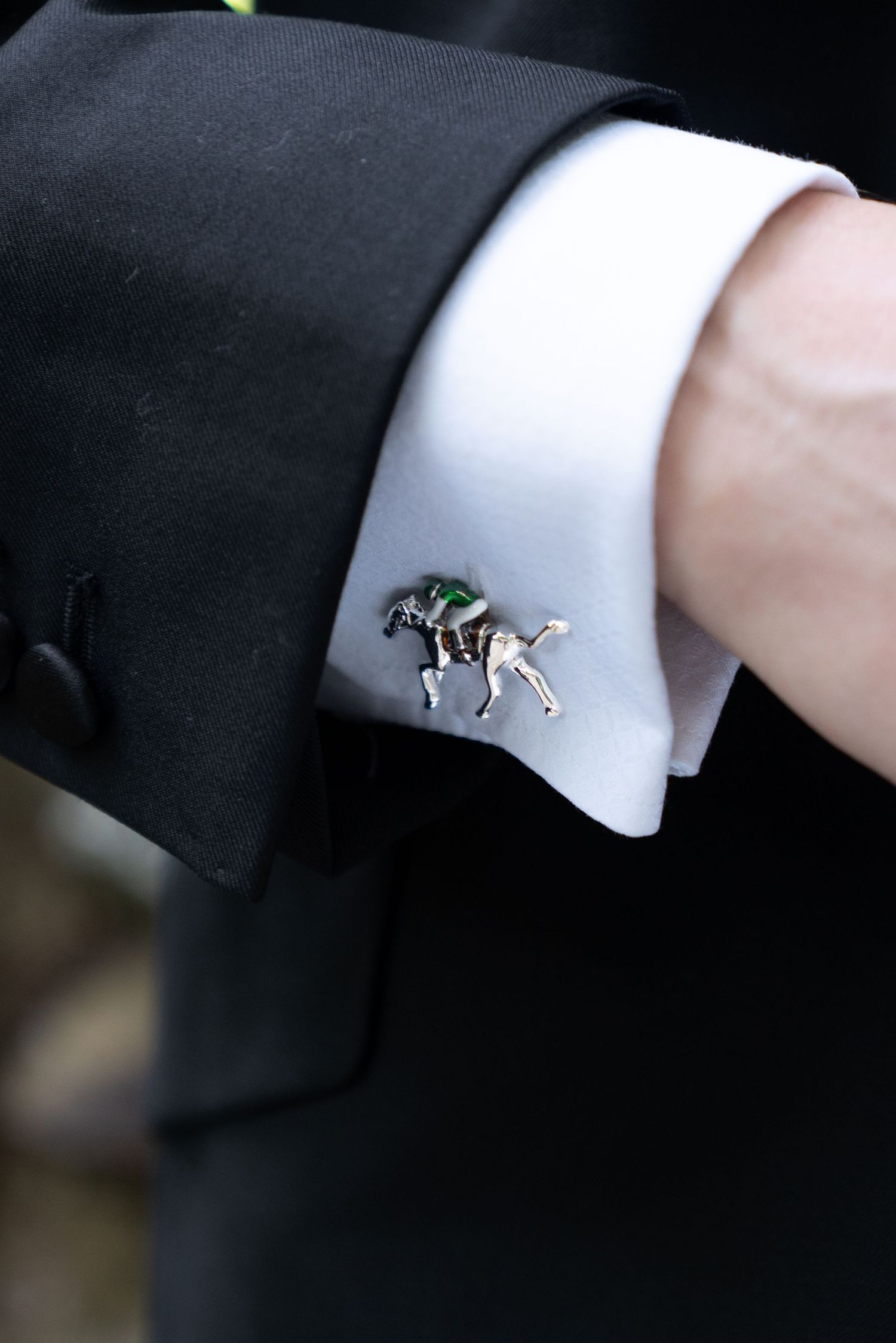 Close-up of groom's cufflink featuring a horse and jockey design on black tuxedo sleeve.