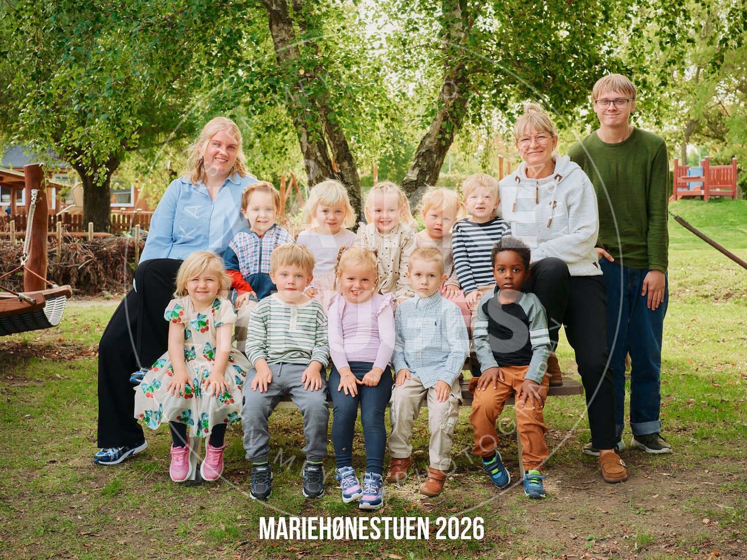 Group photo of children and teachers at Mariehønestuen 2026 kindergarten outdoors under green trees.