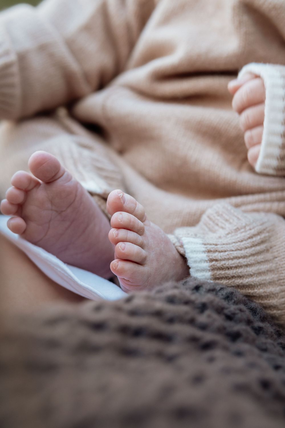 Close-up of tiny newborn baby feet resting on a soft beige knit sweater and brown blanket.