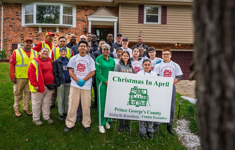Large group of volunteers and workers pose with a Christmas in April Prince Georges County community service sign.