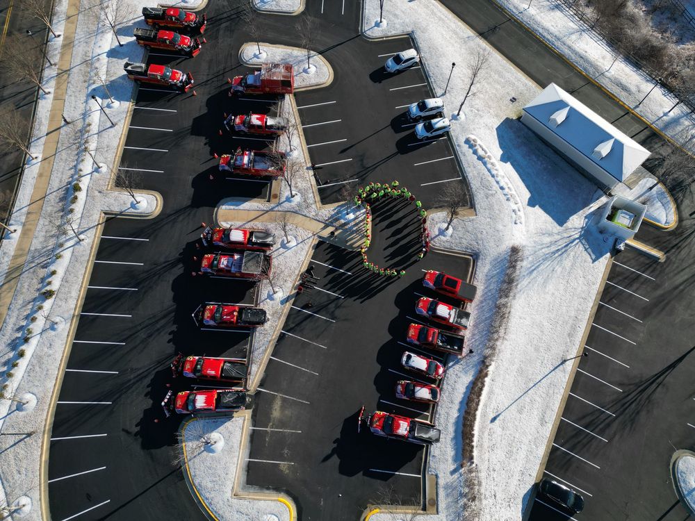 Aerial view of red landscaping trucks neatly parked in a snow-dusted parking lot beside a building in winter.