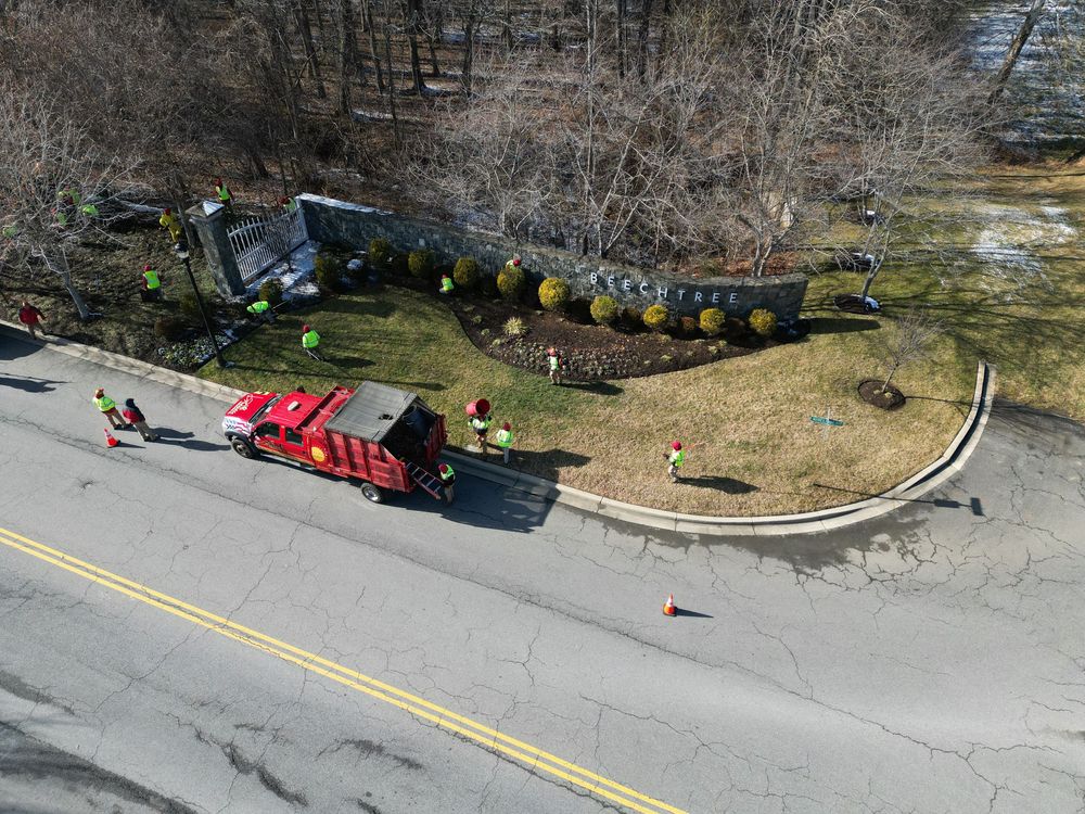 Aerial view of a red truck and crew in safety vests completing landscaping work along a curved roadside garden area.