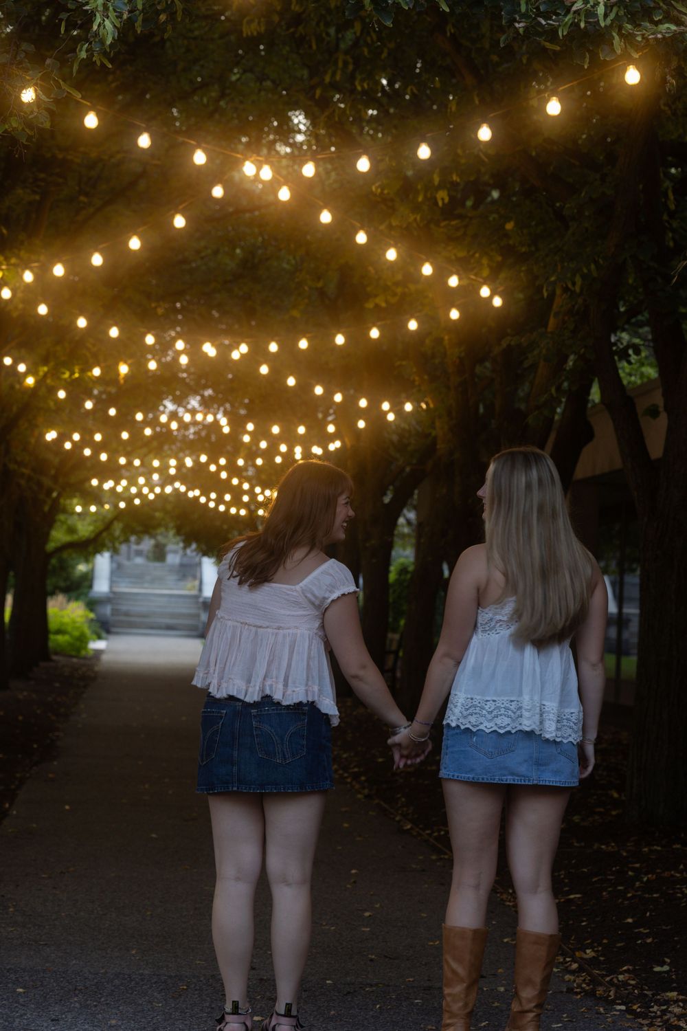 Two women holding hands and facing away under string lights