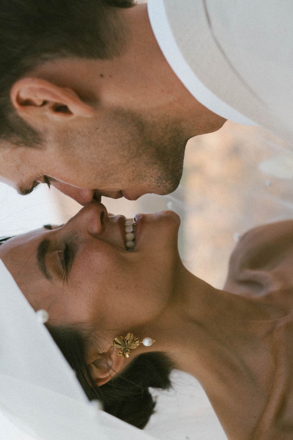 Une mariée et un marié partagent un presque baiser romantique, souriant étroitement sous un voile de mariage blanc.